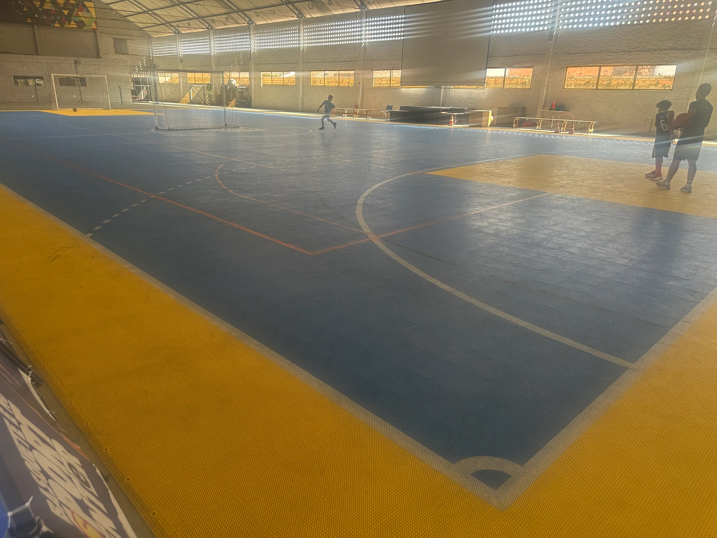 Vista ampla da quadra de futsal coberta com piso azul e traves
