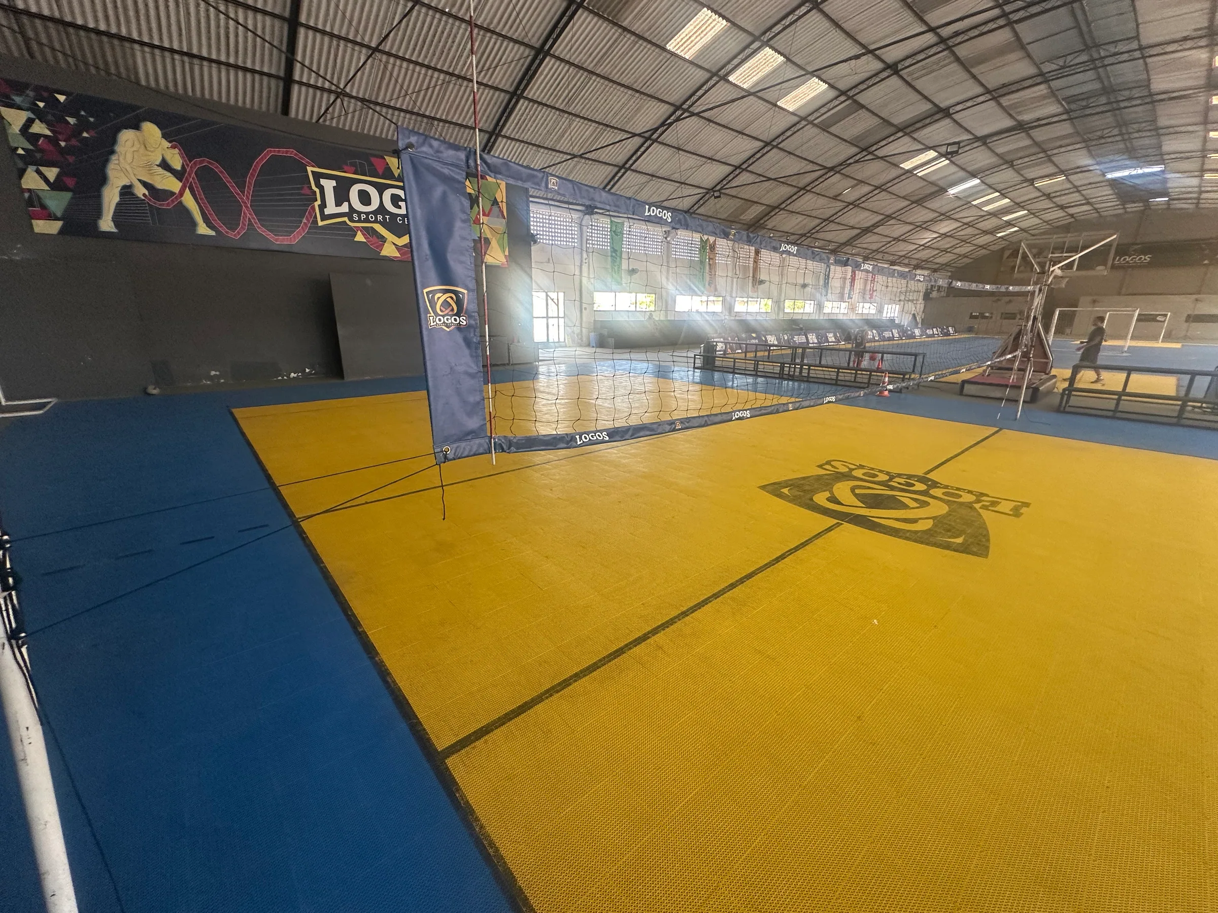 Vista ampla da quadra de vôlei coberta com rede e piso azul e amarelo