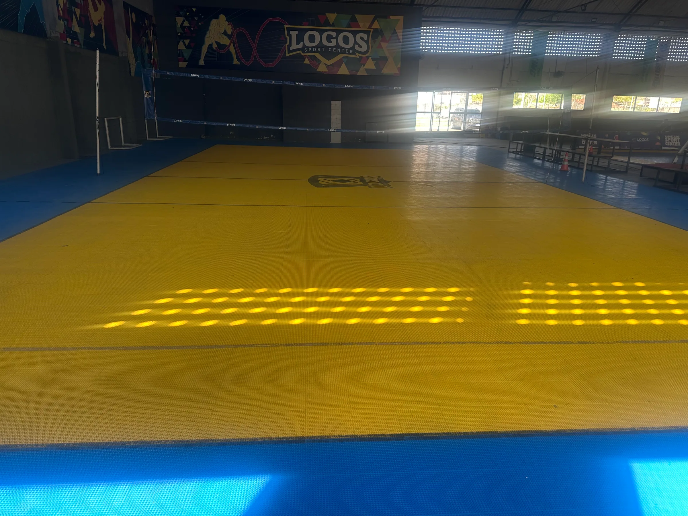 Quadra de vôlei coberta com rede, arquibancada lateral e iluminação natural